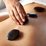 therapist placing a basalt stone on a woman's back, during a hot stone massage