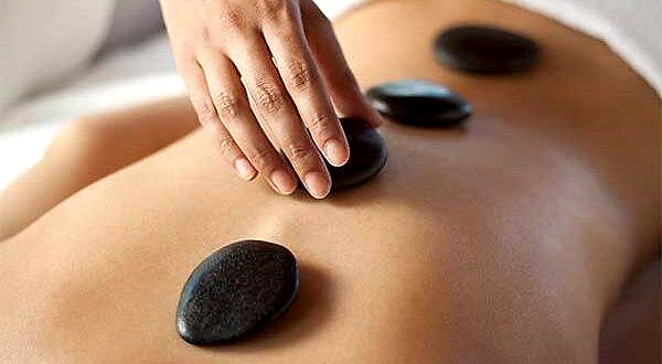 therapist placing a basalt stone on a woman's back, during a hot stone massage