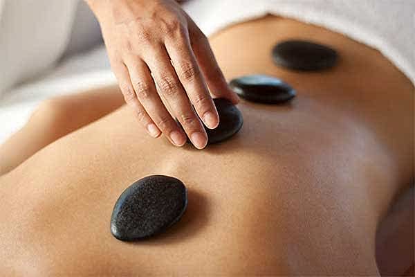 therapist placing a basalt stone on a woman's back, during a hot stone massage