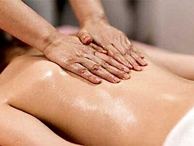 therapist applying massage techniques to a woman's back, during a Thai oil massage