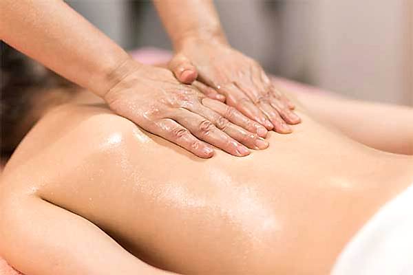 therapist applying massage techniques to a woman's back, during a Thai oil massage